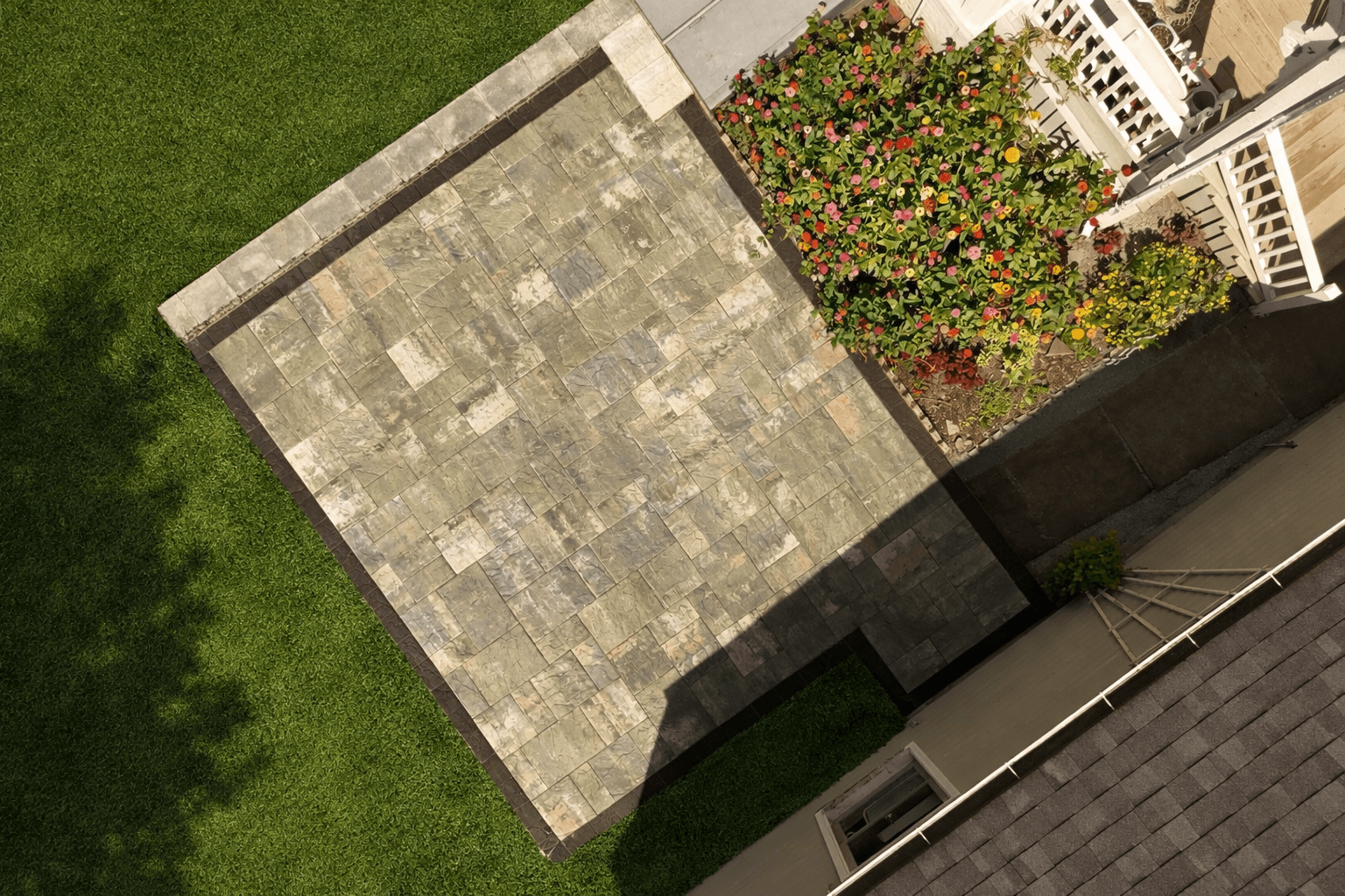 Aerial view of square paver patio with border and surrounding lawn and flower bed