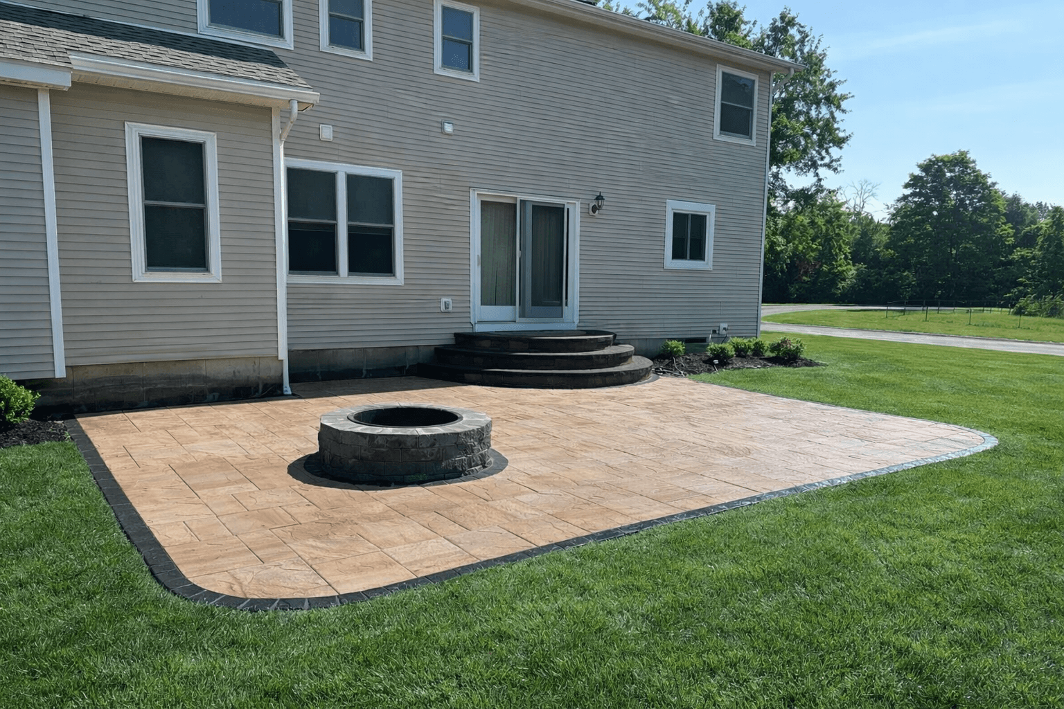 Rectangular stone patio with built-in fire pit behind suburban home