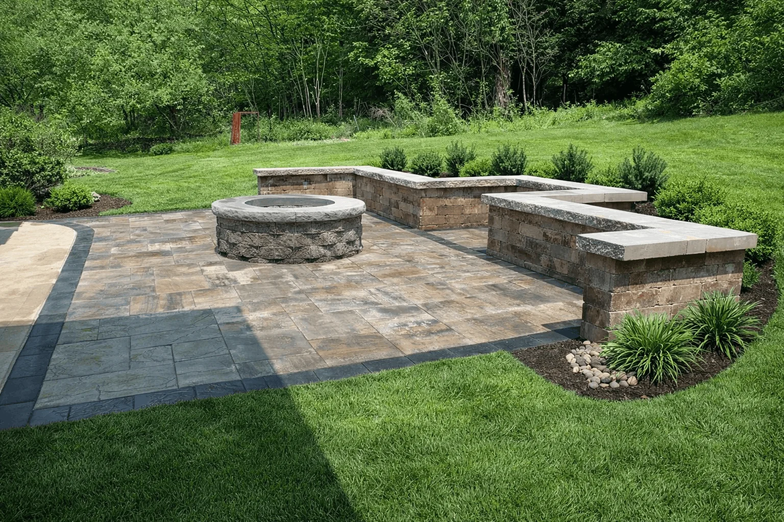 Rectangular paver patio featuring circular fire pit, retaining wall seating, and landscaped lawn