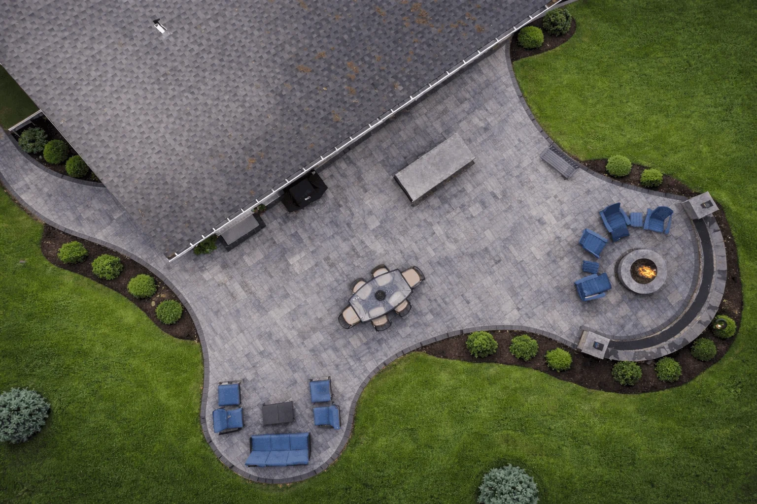 Overhead backyard design featuring curved paver patio, outdoor dining table, and fire pit lounge