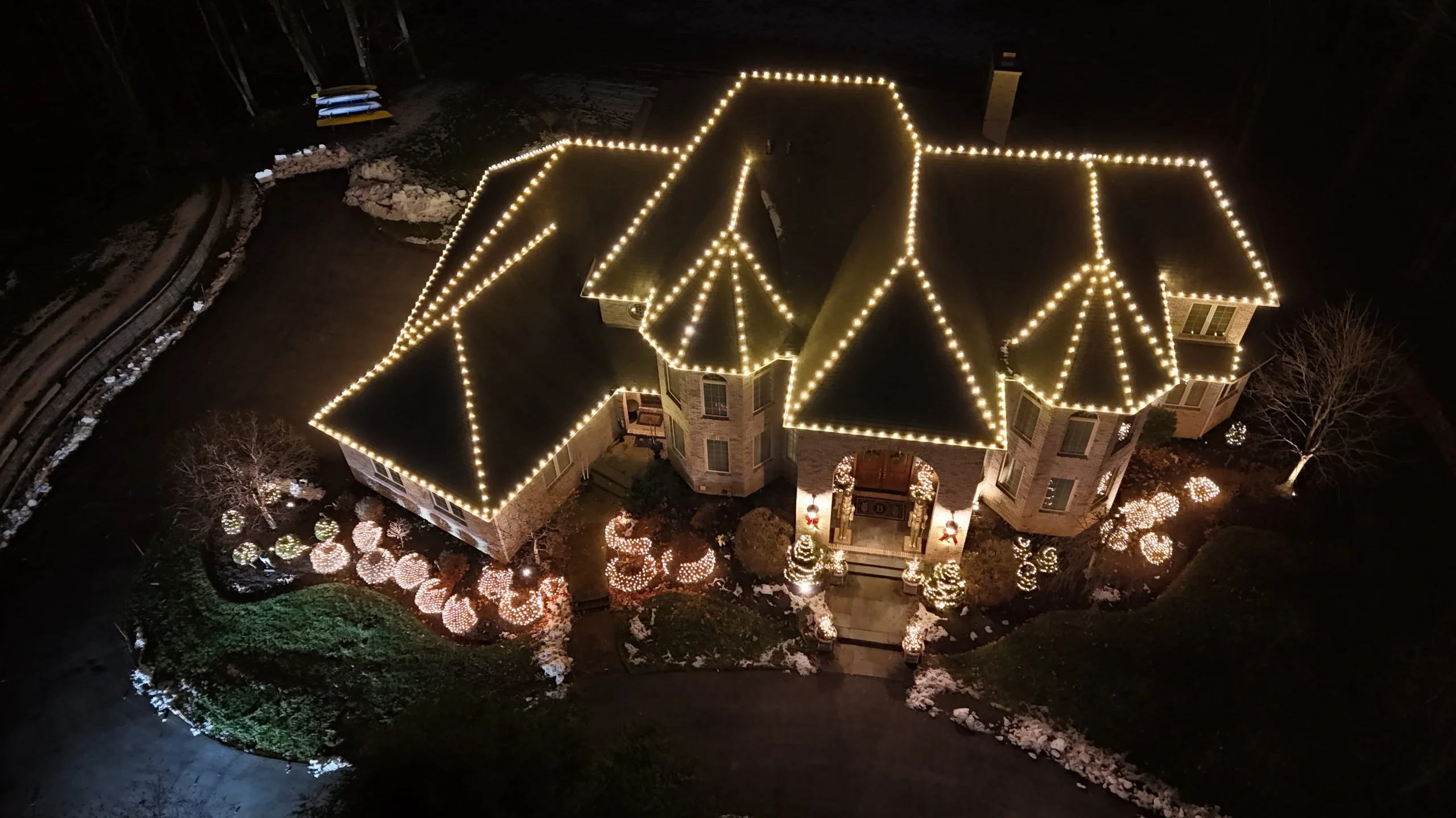 A snowy home decorated with professional Christmas lights and illuminated landscape features during a winter evening