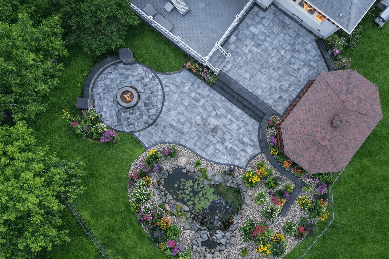 Overhead backyard landscape featuring paver patio, fire pit area, pond, and garden beds.