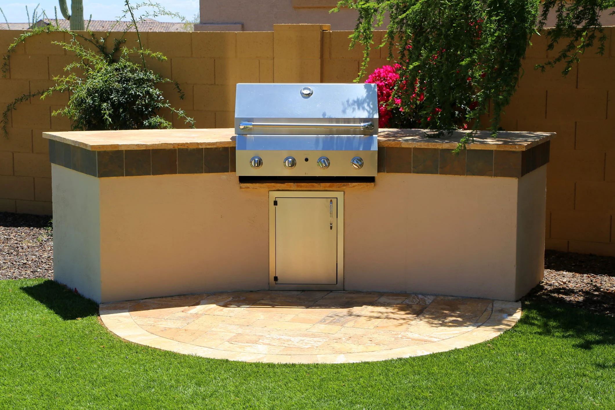 Built-in stainless steel barbecue grill mounted in a stucco outdoor kitchen island with stone countertop.