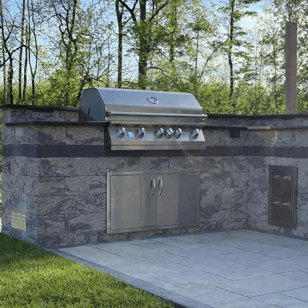 Modern outdoor barbecue setup with stainless steel grill and cabinet storage integrated into a stone patio structure in New York.