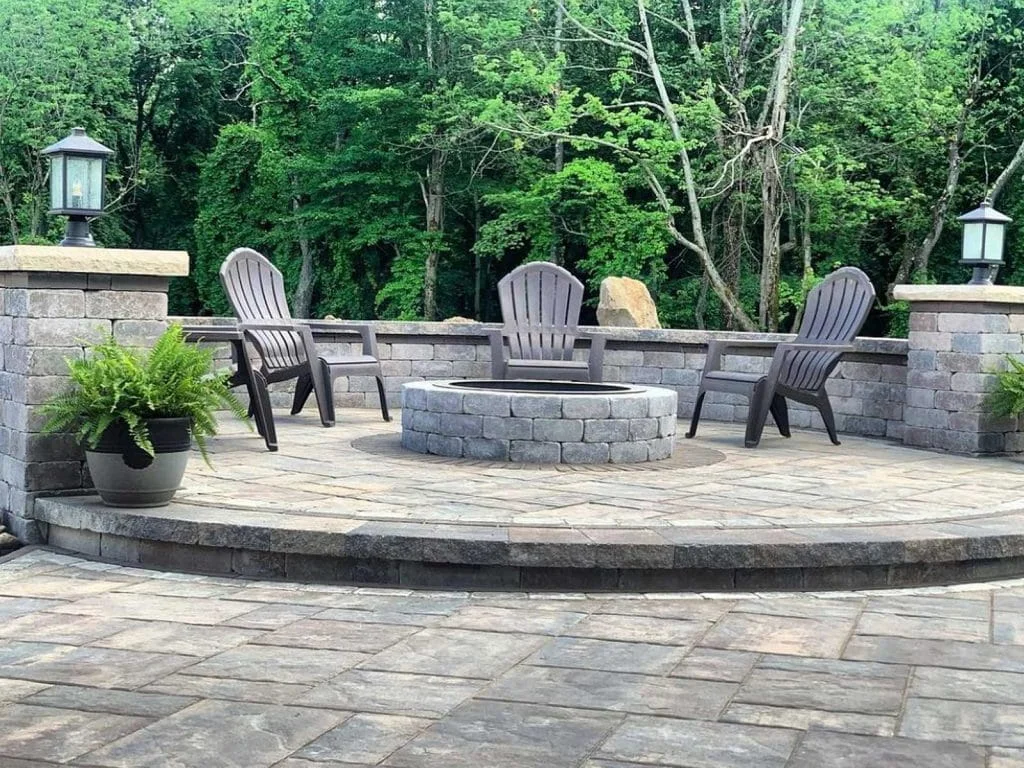 Circular paver patio with stone fire pit and Adirondack chairs surrounded by retaining wall