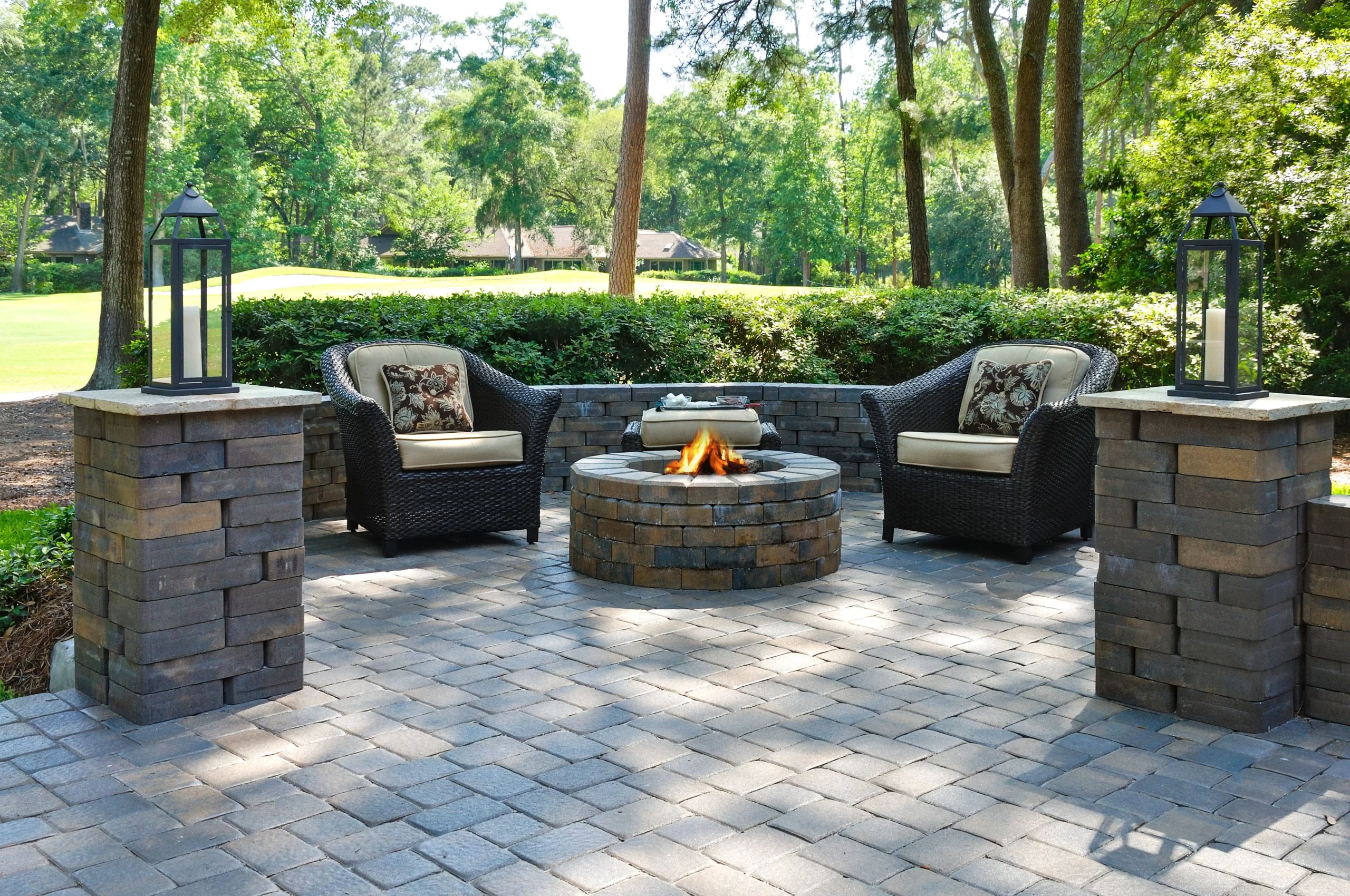 Circular stone fire pit on a paver patio surrounded by wicker chairs and decorative lanterns.