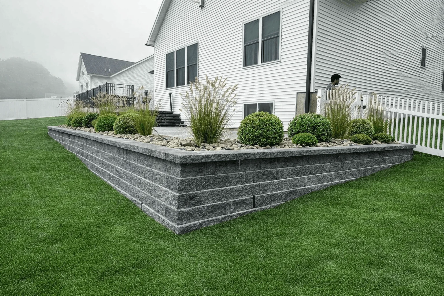 Backyard retaining wall with ornamental grasses, shrubs, and rock mulch border