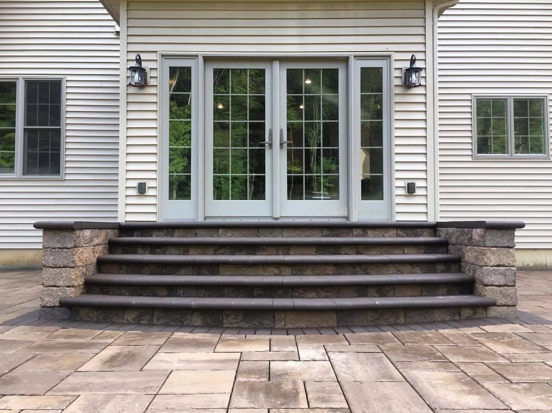 Outdoor paver patio with curved stone steps and French doors providing access to the home in New York.