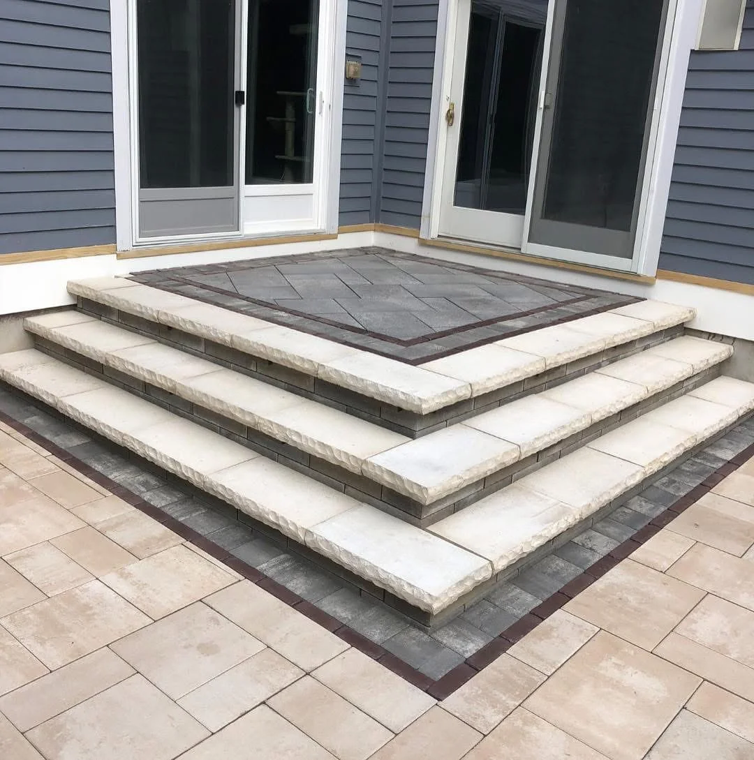 Modern backyard patio featuring layered stone steps and a geometric paver landing by a house in New York.