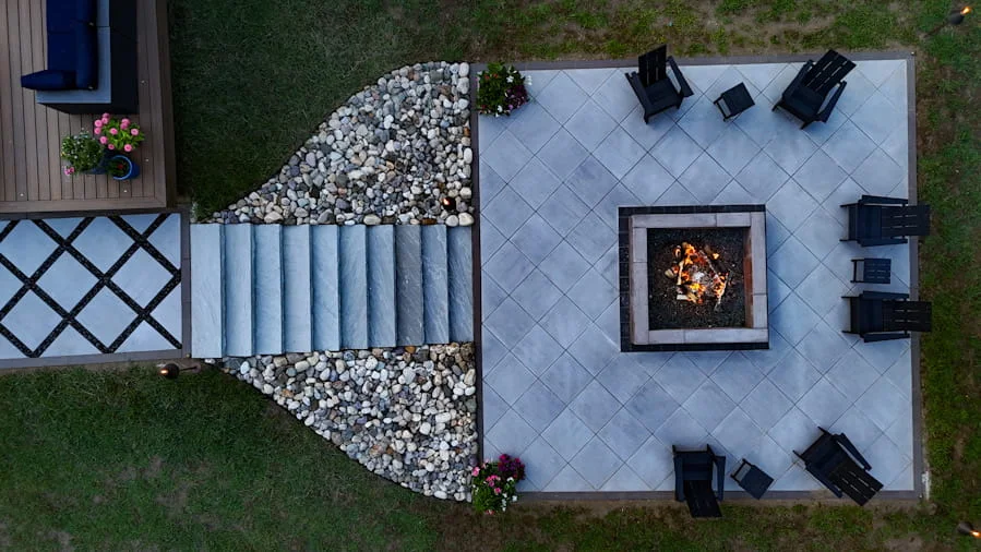 Drone view of a backyard patio featuring a square fire pit, lounge chairs, and decorative stone landscaping.