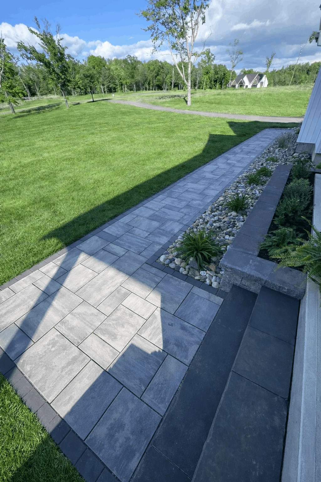 Modern paver walkway with dark border, steps, and decorative river rock drainage bed