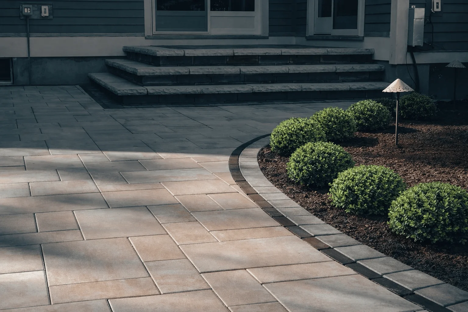 Backyard patio featuring large format pavers, edging stones, and low-maintenance shrub landscaping