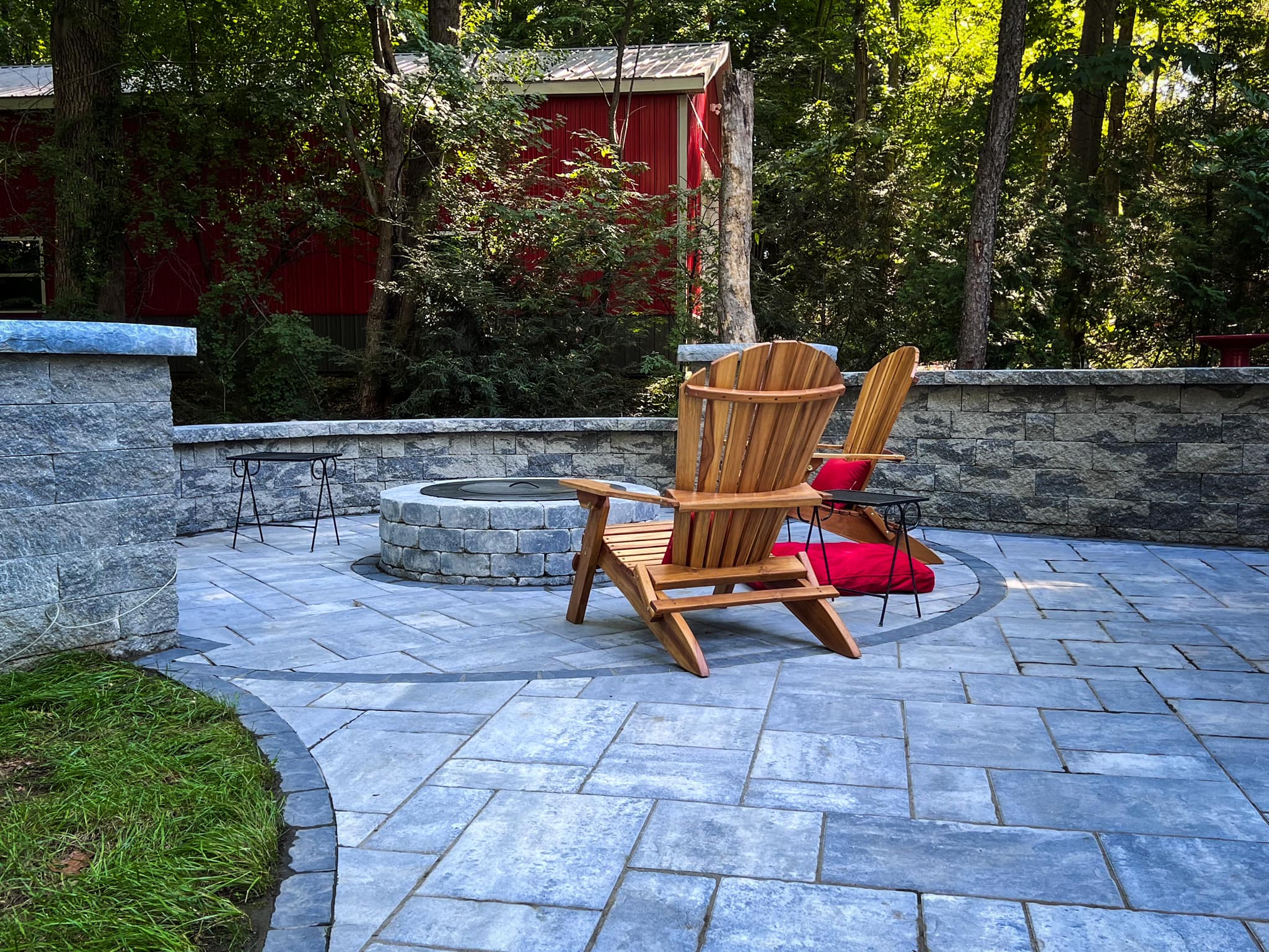 Backyard paver patio with Adirondack chairs, circular fire pit, and stone seating wall